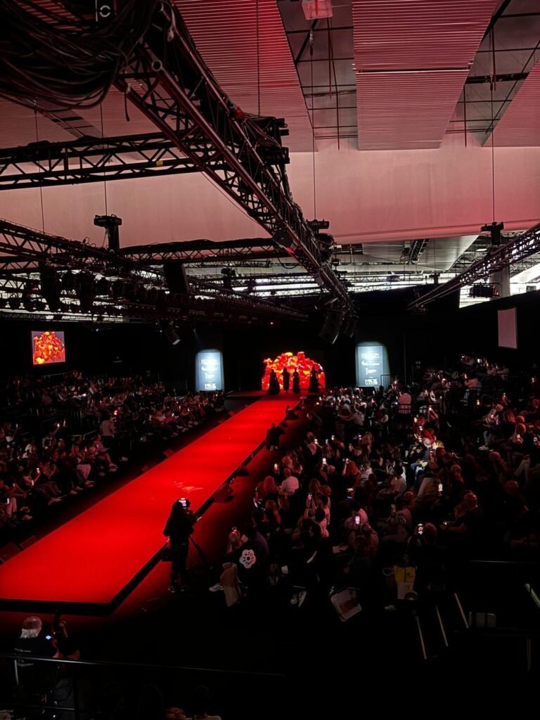 Perspectiva aérea del desfile de moda en el Salón Look 2024, donde un fondo visual vibrante y la iluminación crean un espectáculo cautivador ante un público atento.